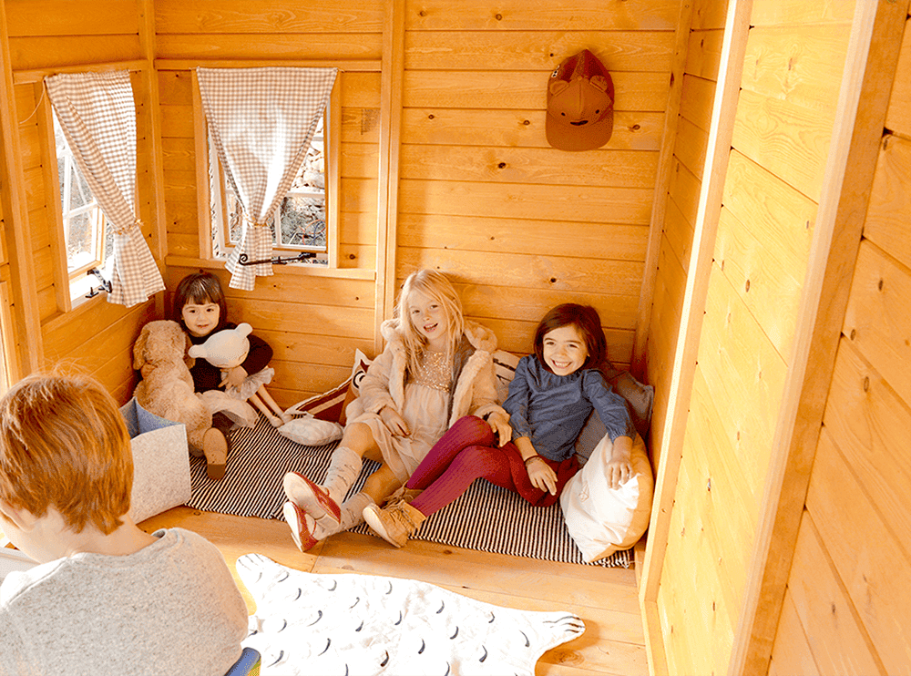 Kinder spielen in einer holzernen Spielhütte im Freien