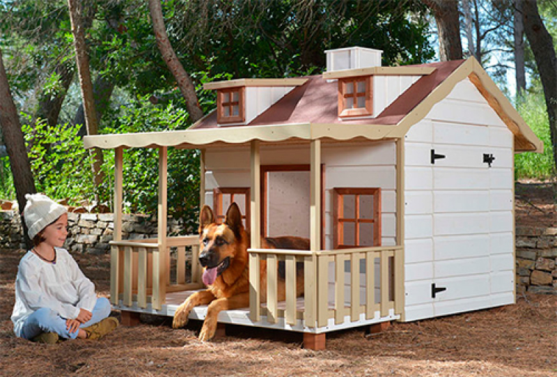Caseta grande de perro de madera blanca con un perro en el porche y una niña mirando